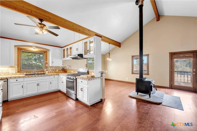 kitchen featuring decorative light fixtures, stainless steel gas stove, a wood stove, sink, and white cabinets