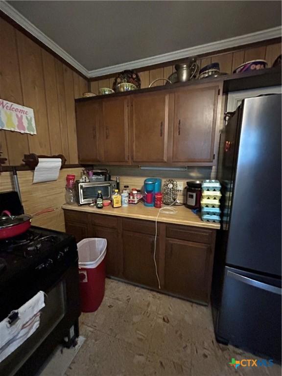 1511 E Constitution St, Victoria, TX 77901 - kitchen with freestanding refrigerator, crown molding, light countertops, and wood walls