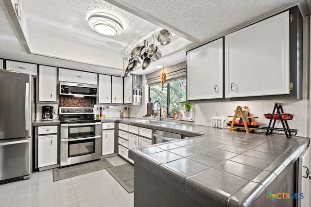 kitchen with tile counters, appliances with stainless steel finishes, and white cabinetry