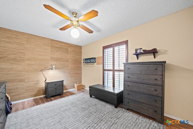 bedroom featuring hardwood / wood-style flooring, a textured ceiling, wooden walls, and ceiling fan