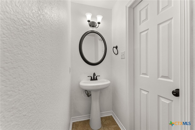 bathroom featuring a textured wall, a sink, and baseboards