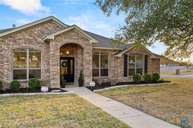 ranch-style home featuring a shingled roof, brick siding, and a front lawn