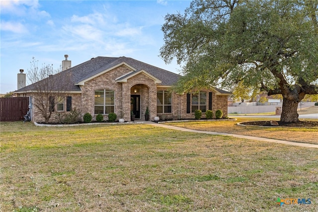 ranch-style home with brick siding, roof with shingles, a chimney, fence, and a front lawn