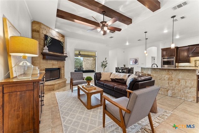 living room featuring a ceiling fan, visible vents, beam ceiling, and a stone fireplace