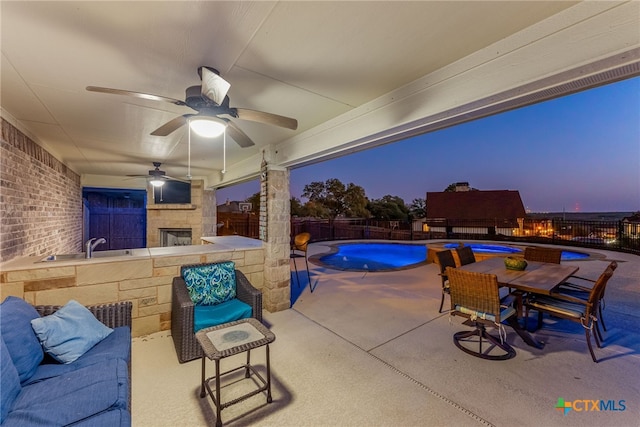 view of patio / terrace with a fenced in pool, a ceiling fan, a fenced backyard, an outdoor fireplace, and a sink