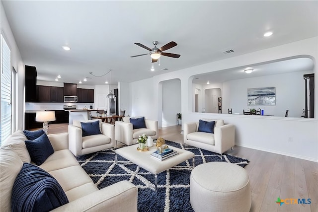 living room with light wood finished floors, visible vents, recessed lighting, arched walkways, and a ceiling fan