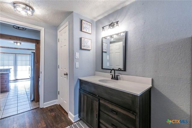 bathroom with vanity, wood finished floors, baseboards, a textured ceiling, and a textured wall
