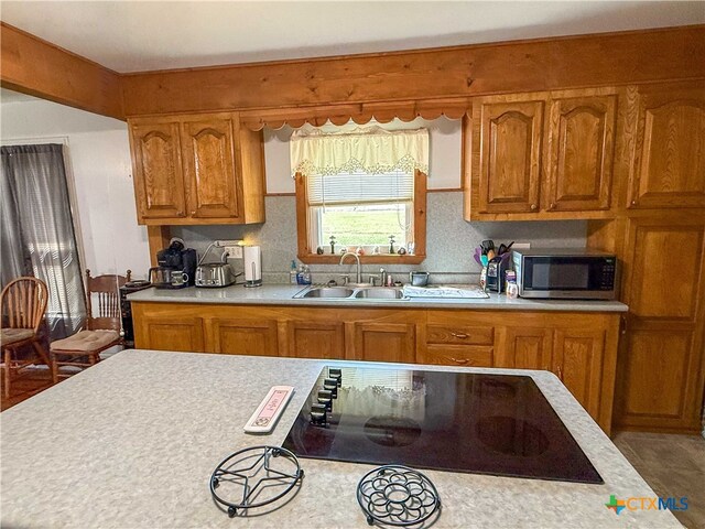 kitchen featuring stainless steel microwave, light countertops, black electric cooktop, and a sink