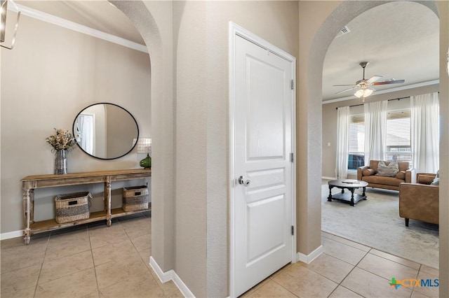 hall featuring light tile patterned flooring, baseboards, arched walkways, and ornamental molding