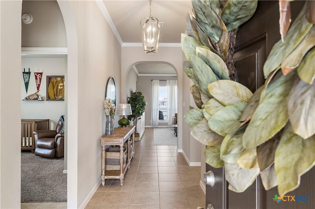 carpeted entryway with arched walkways, a notable chandelier, baseboards, ornamental molding, and tile patterned floors