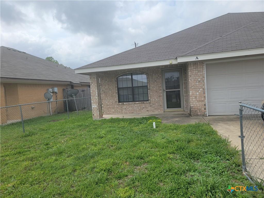 104 Castellon Ct, Killeen, TX 76542 - back of property featuring a lawn, fence, a garage, brick siding, and roof with shingles