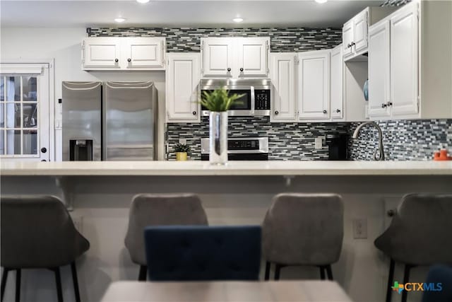 kitchen featuring white cabinets, a breakfast bar area, stainless steel appliances, and decorative backsplash