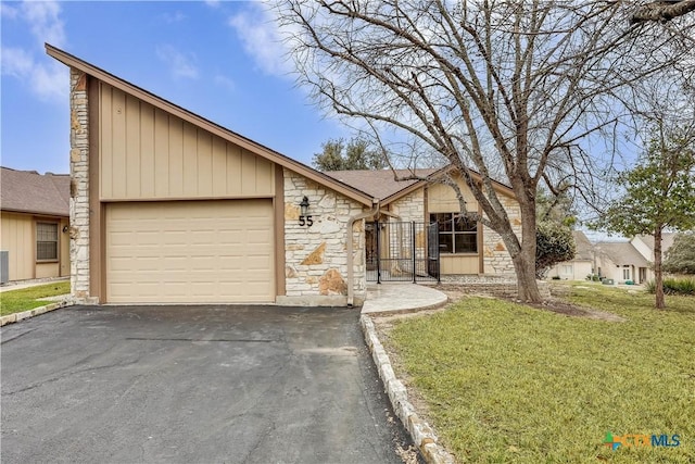 view of front of home with an attached garage, stone siding, driveway, and a front lawn