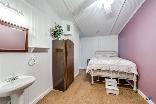 bedroom featuring visible vents, a ceiling fan, a sink, wood finished floors, and baseboards