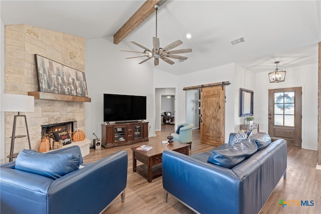 living room with a stone fireplace, light hardwood / wood-style floors, beamed ceiling, and a barn door