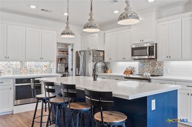 kitchen featuring stainless steel appliances, white cabinets, decorative backsplash, a kitchen island with sink, and pendant lighting