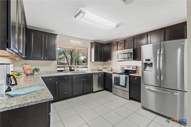 kitchen with light stone countertops, stainless steel appliances, light tile patterned flooring, dark brown cabinets, and sink