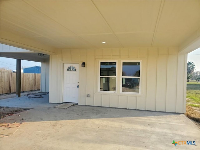 entrance to property with board and batten siding, a patio, and fence