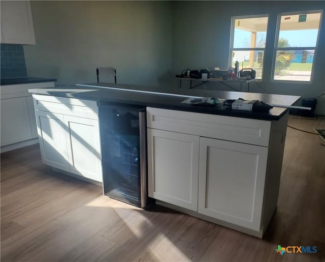 kitchen with wine cooler, light wood finished floors, white cabinetry, and tasteful backsplash