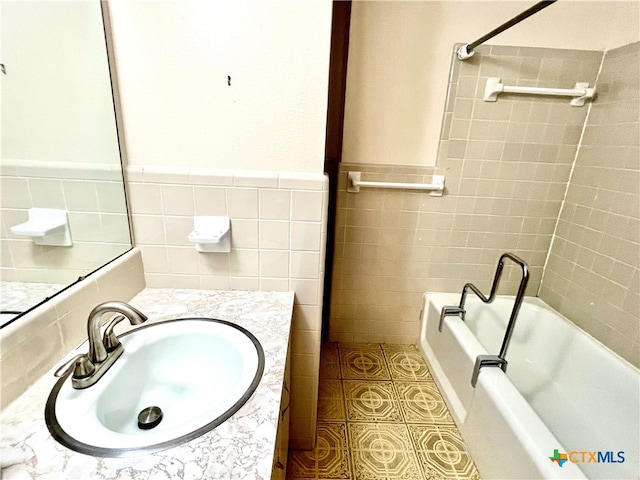 bathroom with tile walls, vanity, and tiled shower / bath