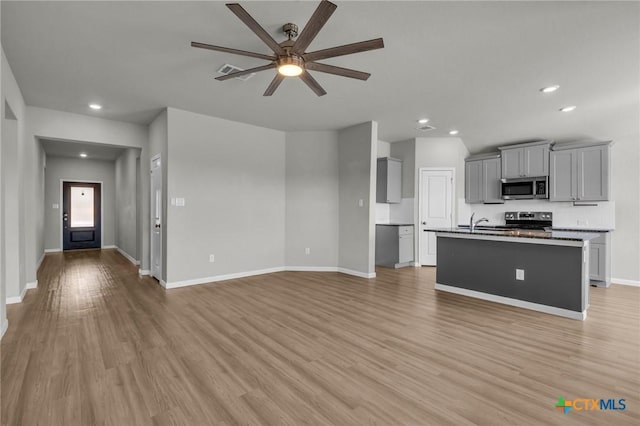 kitchen featuring gray cabinetry, a kitchen island with sink, light hardwood / wood-style flooring, ceiling fan, and stainless steel appliances