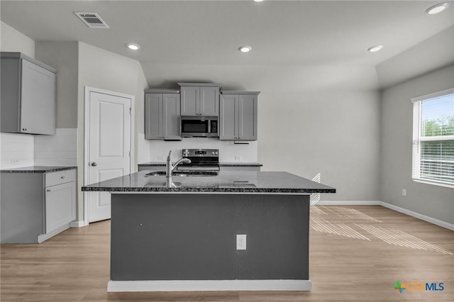 kitchen with a center island with sink, sink, gray cabinets, light wood-type flooring, and appliances with stainless steel finishes