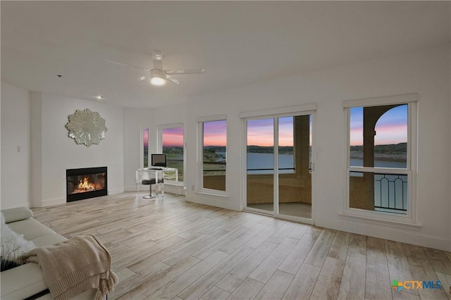 living room with baseboards, wood finished floors, a ceiling fan, and a glass covered fireplace