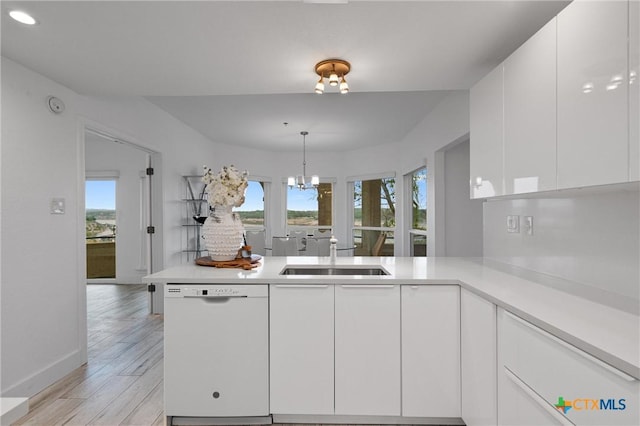kitchen with a sink, white dishwasher, white cabinetry, a peninsula, and light countertops