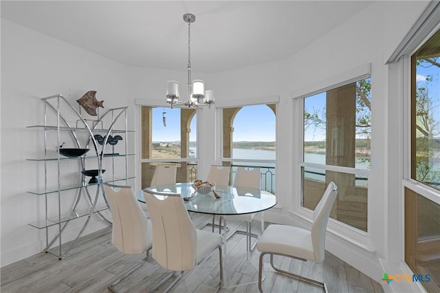 dining space with an inviting chandelier, wood finished floors, a water view, and plenty of natural light