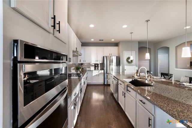 kitchen with sink, white cabinetry, decorative light fixtures, dark stone countertops, and stainless steel appliances