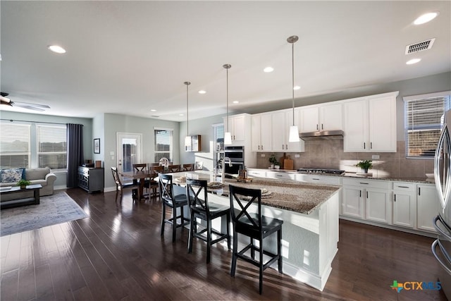 kitchen featuring white cabinetry, dark stone countertops, a kitchen breakfast bar, pendant lighting, and a large island