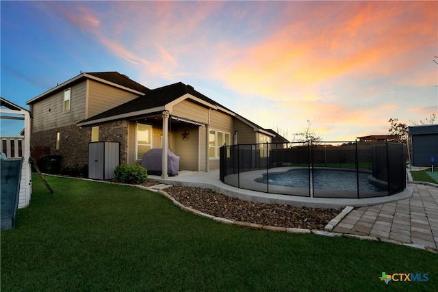 back house at dusk featuring a fenced in pool, a patio, and a yard