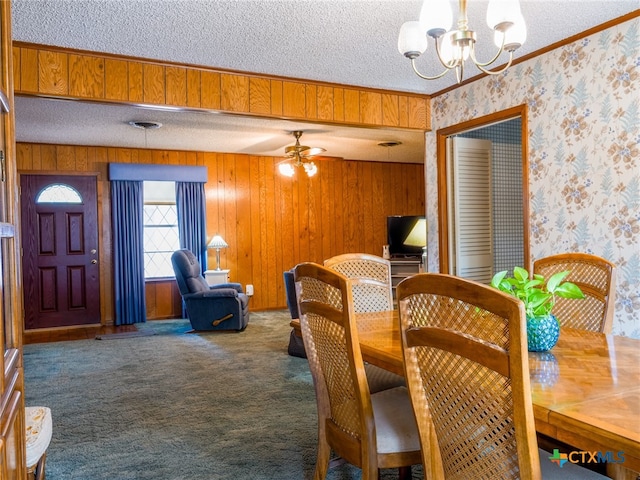 dining space featuring carpet, ceiling fan with notable chandelier, wood walls, and a textured ceiling