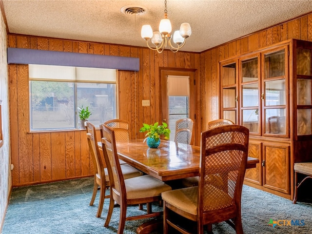 dining room with carpet flooring, wood walls, a textured ceiling, and a notable chandelier