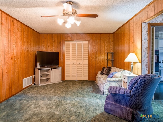 living room with ornamental molding, dark carpet, a textured ceiling, wood walls, and ceiling fan