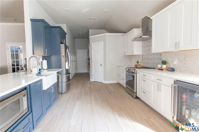 kitchen featuring stainless steel appliances, beverage cooler, sink, blue cabinetry, and wall chimney range hood