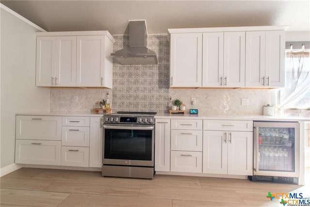 kitchen with stainless steel electric stove, wall chimney range hood, white cabinetry, and wine cooler