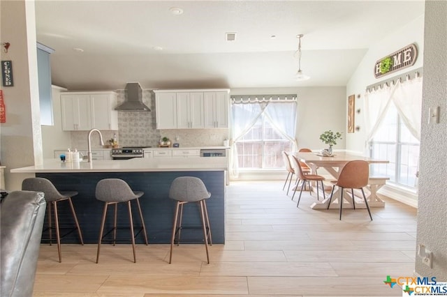 kitchen with white cabinetry, wall chimney range hood, pendant lighting, and plenty of natural light