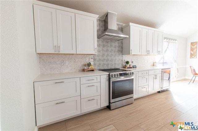 kitchen with white cabinets, wall chimney exhaust hood, stainless steel range oven, backsplash, and light hardwood / wood-style flooring