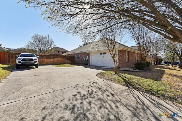 view of side of property featuring an attached garage, fence, brick siding, and driveway