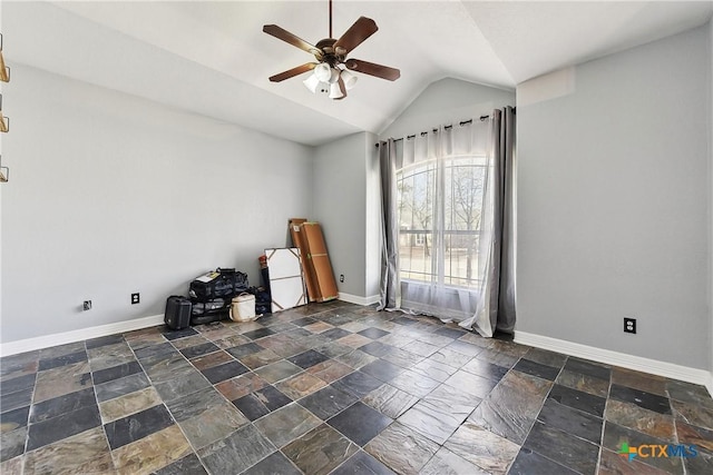 empty room featuring lofted ceiling, stone tile floors, a ceiling fan, and baseboards