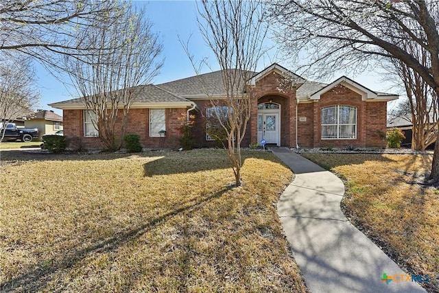 ranch-style home featuring brick siding, a shingled roof, and a front yard