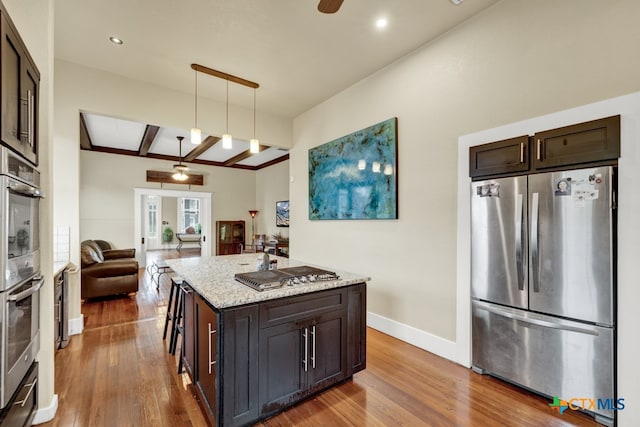 kitchen with a center island with sink, a breakfast bar, appliances with stainless steel finishes, wood-type flooring, and pendant lighting