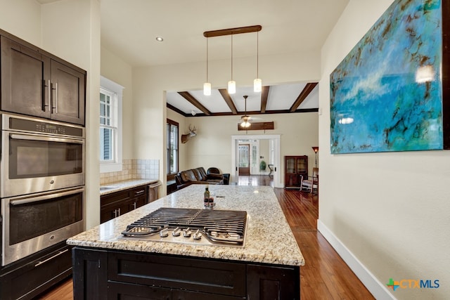 kitchen featuring dark hardwood / wood-style flooring, hanging light fixtures, tasteful backsplash, light stone countertops, and appliances with stainless steel finishes