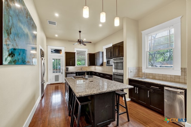 kitchen with dark brown cabinetry, a kitchen breakfast bar, decorative backsplash, and an island with sink