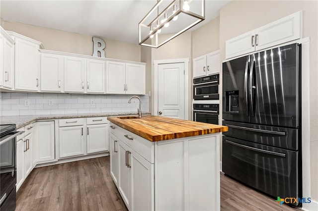 kitchen with fridge with ice dispenser, white cabinets, an island with sink, and wood counters