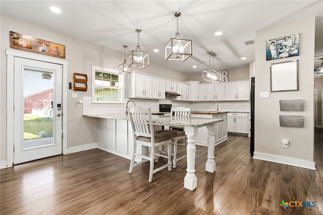 kitchen with tasteful backsplash, white cabinetry, dark hardwood / wood-style flooring, hanging light fixtures, and a kitchen breakfast bar