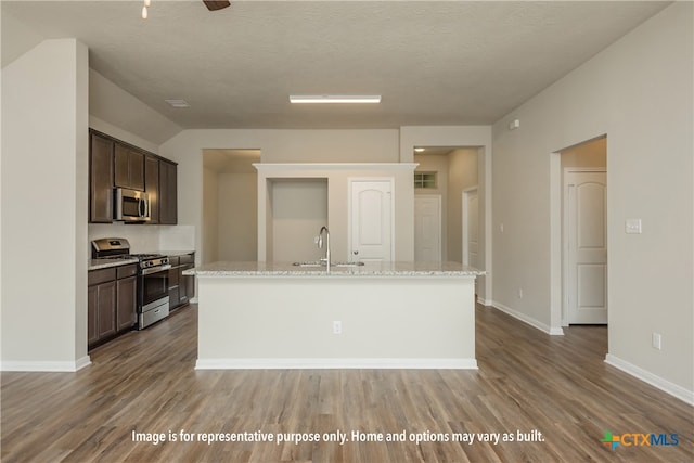 kitchen featuring dark brown cabinets, hardwood / wood-style floors, stainless steel appliances, and a center island with sink