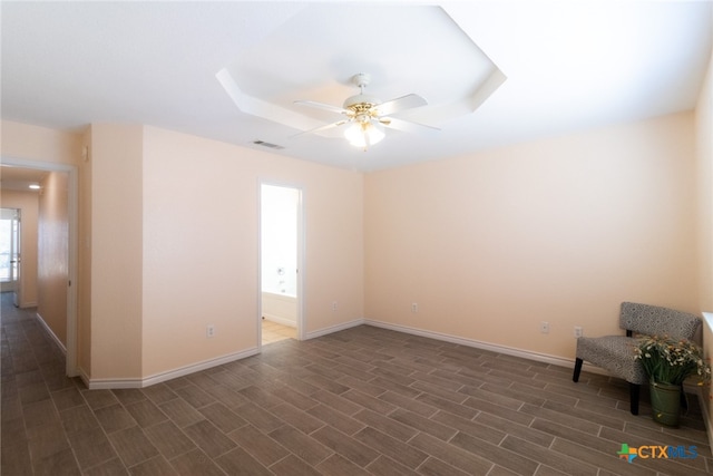 empty room featuring dark hardwood / wood-style flooring, ceiling fan, and a raised ceiling