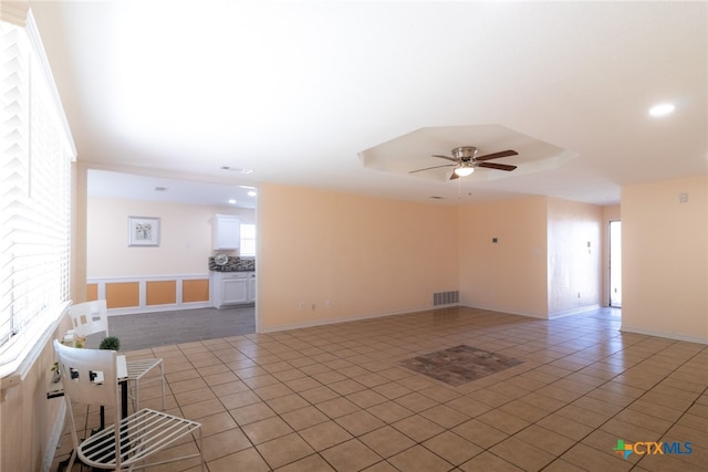 spare room with tile patterned flooring, a raised ceiling, a healthy amount of sunlight, and ceiling fan